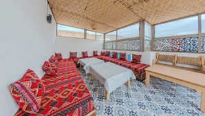 A room with a woven ceiling, large windows, patterned bedding, and a tiled floor. - House Aisha (Tamraght)