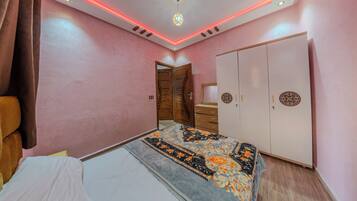 Quarto com paredes cor-de-rosa, cama com colcha estampada, guarda-roupa e iluminação vermelha no teto.