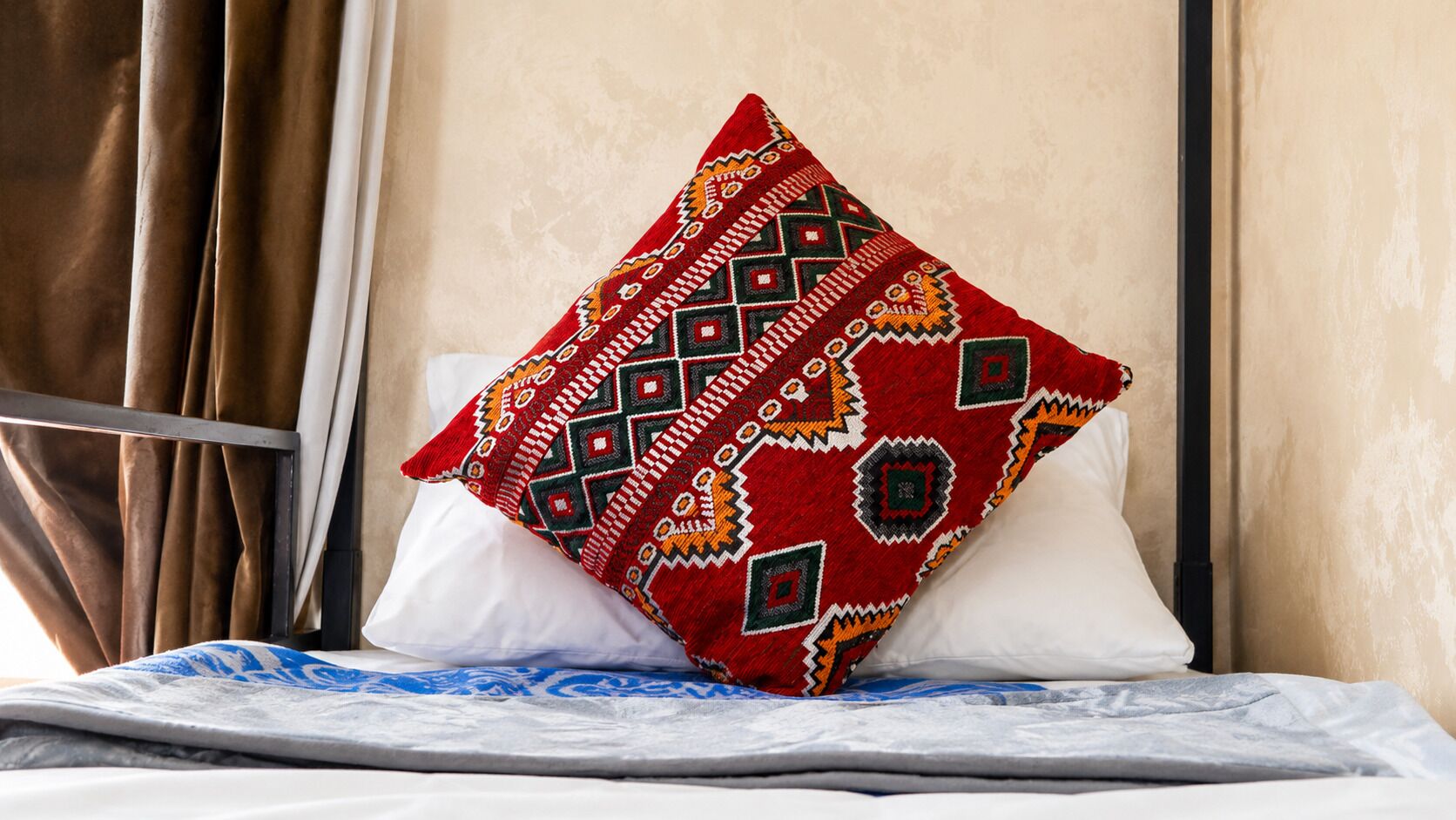 Een bed met een wit kussen en een decoratief kussen met een geometrisch patroon.