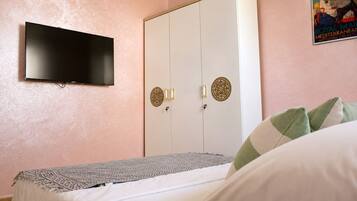 Un dormitorio con cama, armario, televisor montado en la pared y un cartel en la pared.