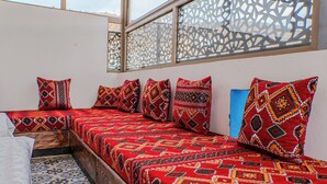 A room with a bed covered in patterned bedding, a window with decorative lattice, and a tiled floor. - House Aisha (Tamraght)