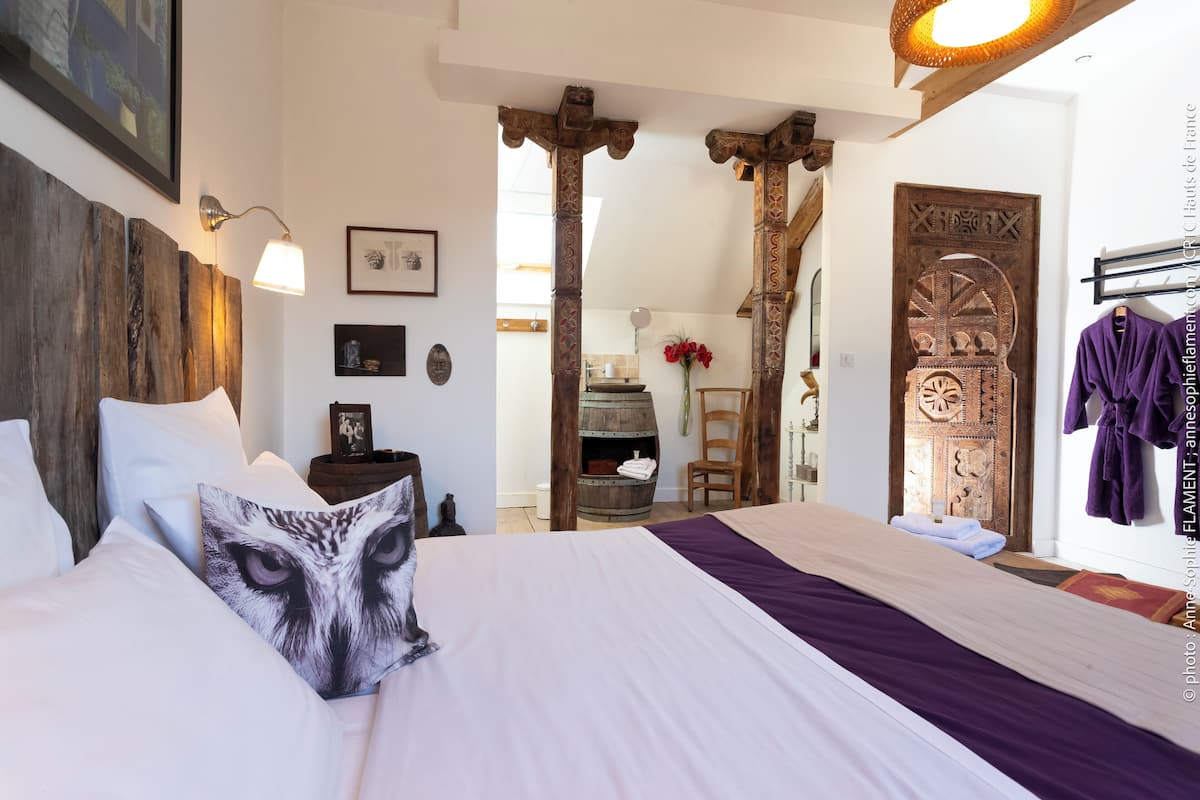 A bedroom with a large bed, a wooden headboard, a wooden door with intricate carvings, and a hanging robe rack.