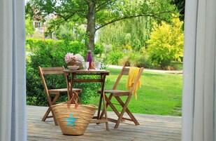 An outdoor wooden deck with a table and chairs, a woven basket, and a vase of flowers.