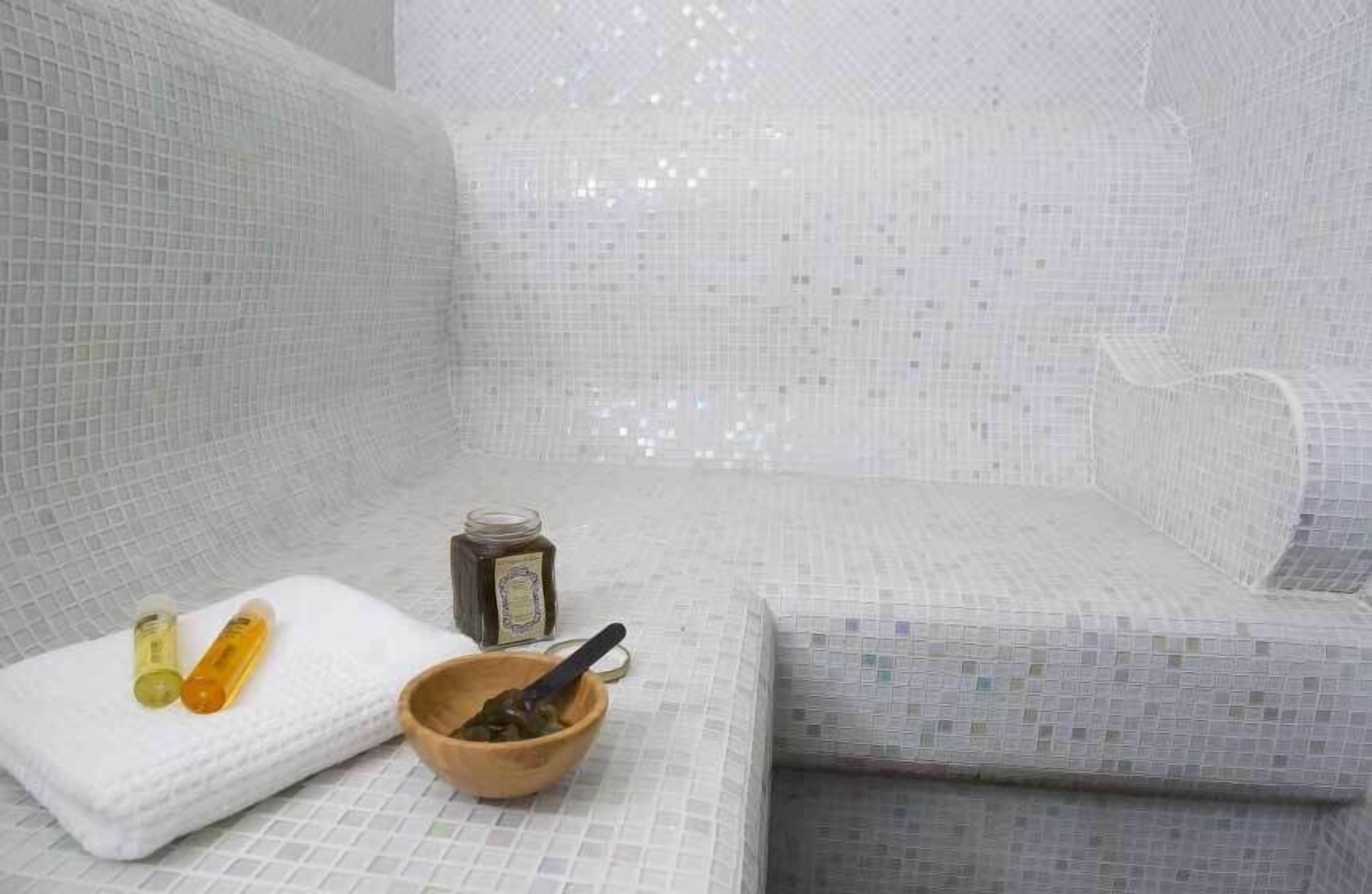 Une salle de bain avec un sol et des murs carrelés, une serviette blanche, un bol en bois et deux bouteilles.