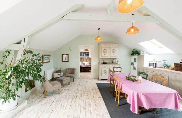 A cozy loft-style room with a dining area, kitchenette, and a large window.