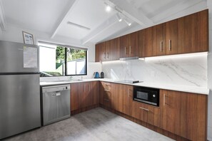 A modern kitchen with wooden cabinets, a stainless steel refrigerator, a Bosch dishwasher, and a Bosch oven. - Welcome to Malibu - Your Laid-Back Straddie Beach Getaway (Point Lookout)