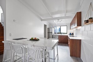 A modern kitchen with white cabinetry, a marble countertop, and a dining area with white chairs. - Welcome to Malibu - Your Laid-Back Straddie Beach Getaway (Point Lookout)