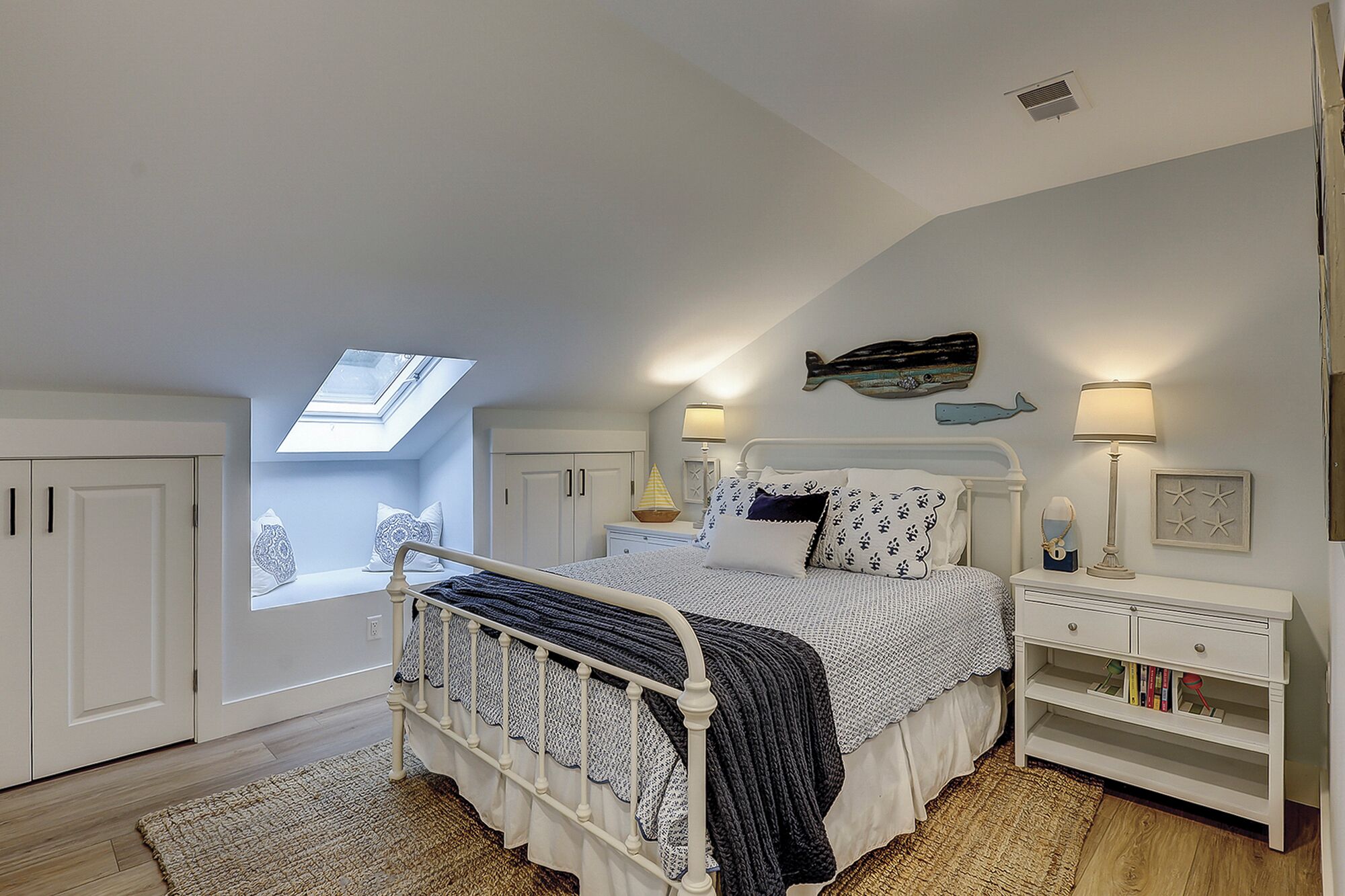 A bedroom with a skylight, a bed with patterned bedding, a nightstand with a lamp, and a bookshelf.