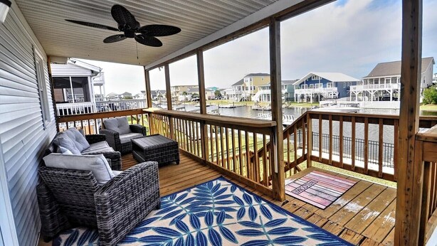 A covered deck with wicker furniture and a view of houses across a body of water. - 3-bedroom canal home in delightful Ocean Isle Beach with boat dock. (Ocean Isle Beach)