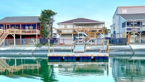 A waterfront property with a dock, a staircase leading to a balcony, and a building with a balcony and a covered porch. - 3-bedroom canal home in delightful Ocean Isle Beach with boat dock. (Ocean Isle Beach)