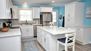 A modern kitchen with white cabinetry, a stainless steel refrigerator, and a blue accent wall. - 3-bedroom canal home in delightful Ocean Isle Beach with boat dock. (Ocean Isle Beach)