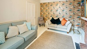 A living room with a grey sofa, a white armchair, and a patterned wallpaper. - Host and Stay Prospect Rise (Hastings)