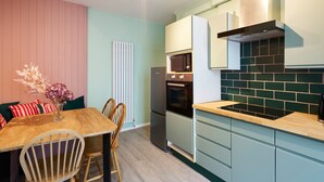 A compact kitchen with a dining area, featuring a wooden table, chairs, a refrigerator, a microwave, and a stove. - Host and Stay Prospect Rise (Hastings)