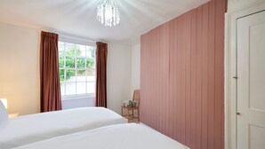 A bedroom with two beds, a window with curtains, a wooden chair, and a white door. - Host and Stay Prospect Rise (Hastings)