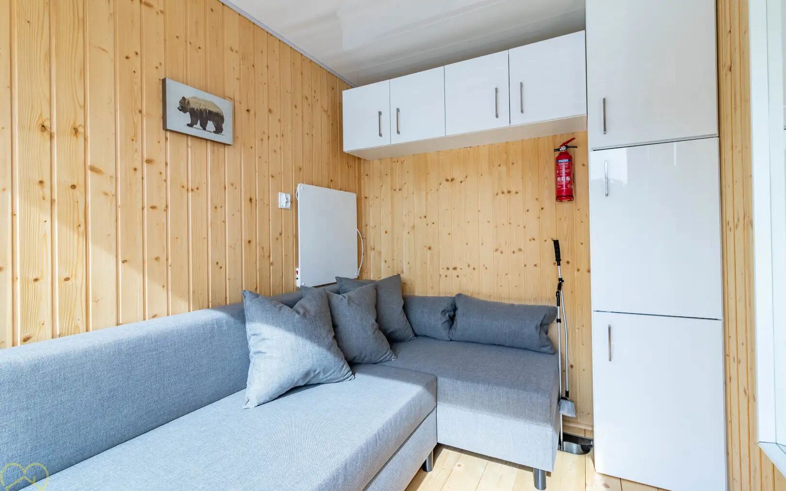 A modern room with a grey sectional sofa, white cabinets, and a wooden wall with a bear picture.