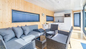 A modern interior with a wooden wall, a sofa, wicker chairs, and a kitchen area. - The Saltkrokan Houseboat in the Archipelago of Southern Sweden (Blankaholm)