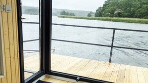 A room with a large window overlooking a river, wooden flooring, and a black mat at the entrance. - The Saltkrokan Houseboat in the Archipelago of Southern Sweden (Blankaholm)