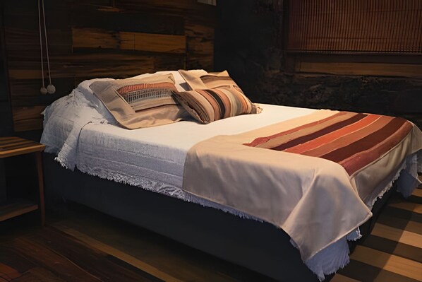 Una cama con edredón blanco y manta a rayas, cabecera de madera y suelo de madera.