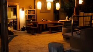 Un espacio interior con una mesa de madera y bancos, una chimenea y lámparas colgantes.