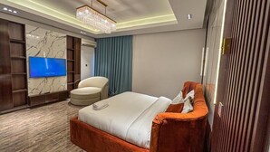 Una habitació d'hotel moderna amb un llit gran, una zona d'estar amb una cadira, una televisió i un panell decoratiu a la paret.