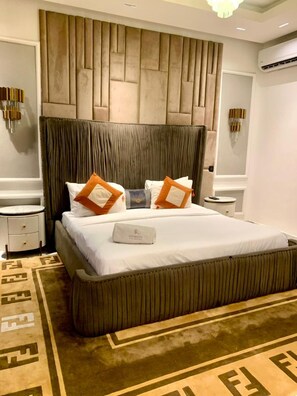 A neatly arranged hotel room with a large bed, a headboard with a textured design, two bedside tables, and a decorative wall panel. - Sujimoto Serviced Apartments (Lagos)