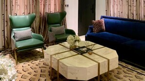 Un saló modern amb un sofà blau, dues butaques verdes, una taula de centre de marbre i cortines amb dibuixos.