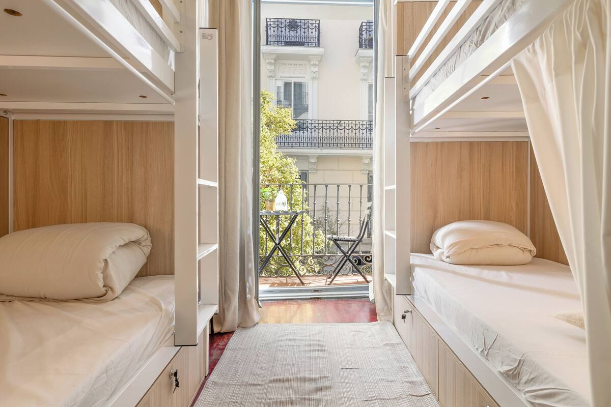 A compact room with two bunk beds, a small balcony, and a view of a building with balconies.