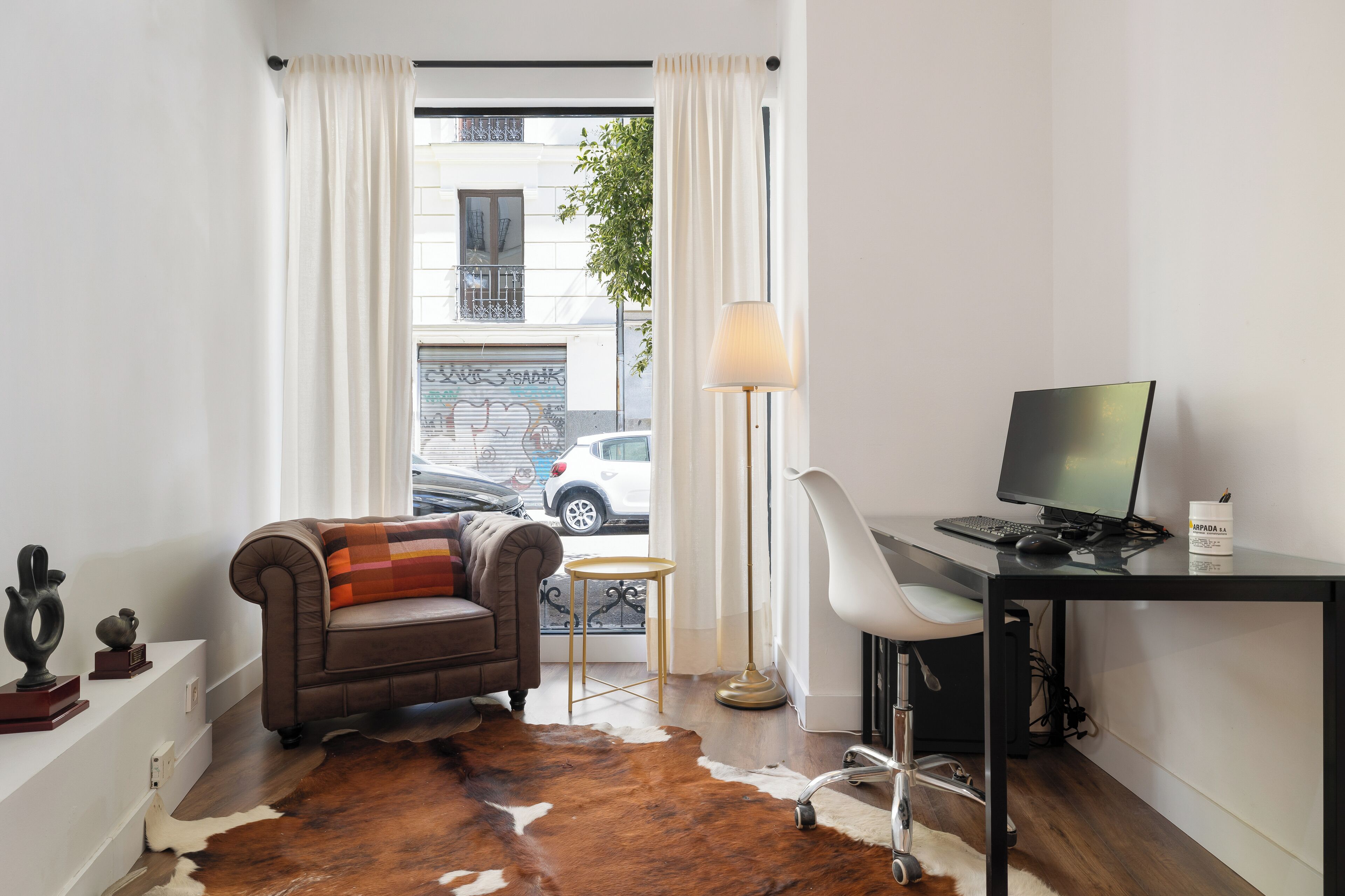 A modern room with a leather sofa, a desk with a computer, a cowhide rug, and a view of the street outside.