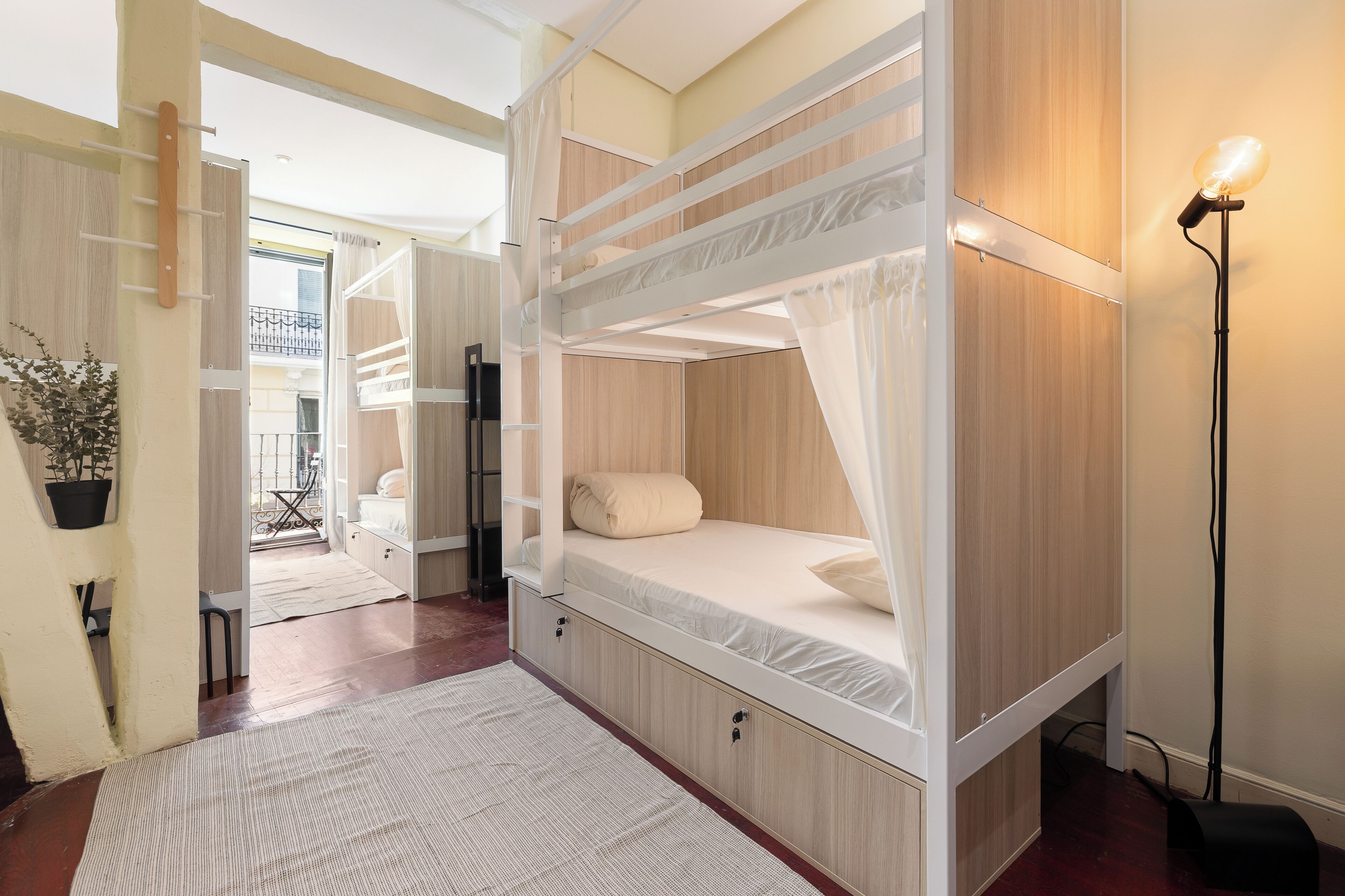 A bunk bed room with a canopy, a bedside table, a floor lamp, and a view of the outside balcony.