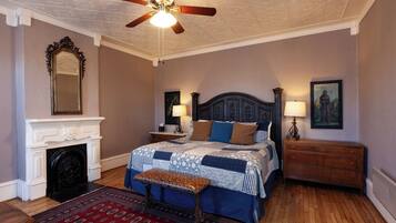 A bedroom with a bed, a fireplace, a ceiling fan, and a nightstand.