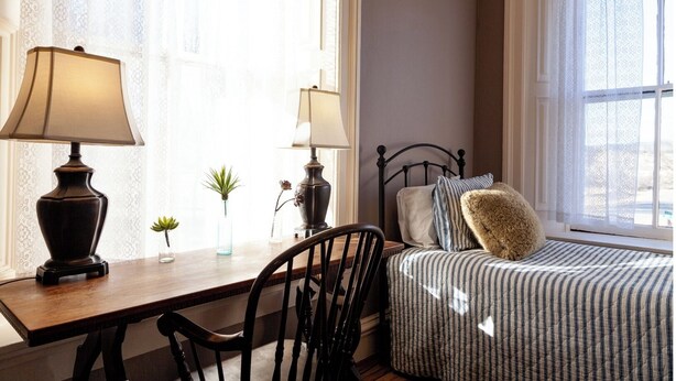Une chambre à coucher avec un lit, une table de chevet avec des lampes, une chaise et une fenêtre avec des rideaux.