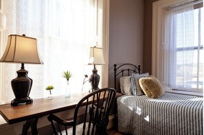 Un dormitorio con cama, una mesita de noche con lámparas, una silla y un ventanal con cortinas.
