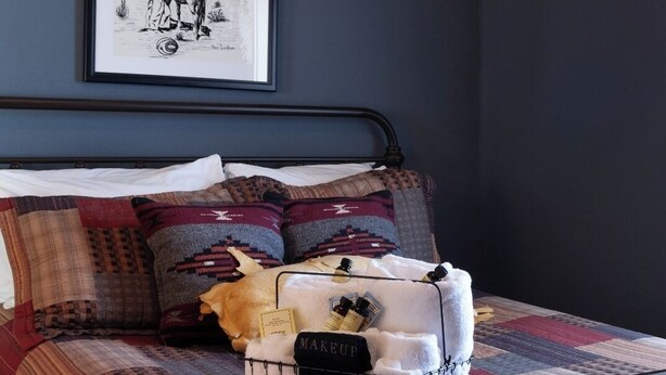 A bed with a quilt, pillows, and a makeup basket. - Fred Lambert - Historic Hotel Room (Cimarron)