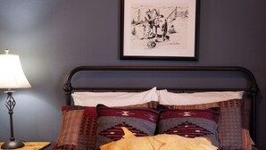 A bed with a patterned quilt, two pillows, and a framed picture on the wall. - Fred Lambert - Historic Hotel Room (Cimarron)