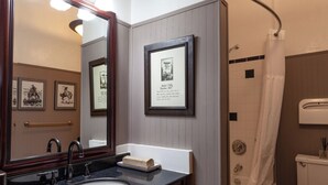 A bathroom with a sink, mirror, framed pictures, and a shower. - Fred Lambert - Historic Hotel Room (Cimarron)
