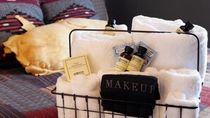 A toiletry basket with a black towel labeled "MAKEUP" and three bottles of Bigelow products, including soap and shampoo, on a bed with patterned bedding and pillows. - Fred Lambert - Historic Hotel Room (Cimarron)