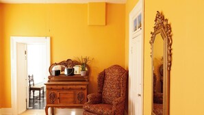 A room with a wooden dresser, a patterned armchair, and a large ornate mirror on a yellow wall. - William F. Cody - Historic Hotel Room (Cimarron)