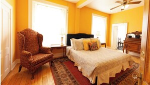 A bedroom with a large bed, a chair, a dresser, and a ceiling fan. - William F. Cody - Historic Hotel Room (Cimarron)
