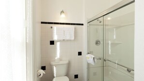 A bathroom with a toilet, a glass shower enclosure, and a towel rack. - William F. Cody - Historic Hotel Room (Cimarron)
