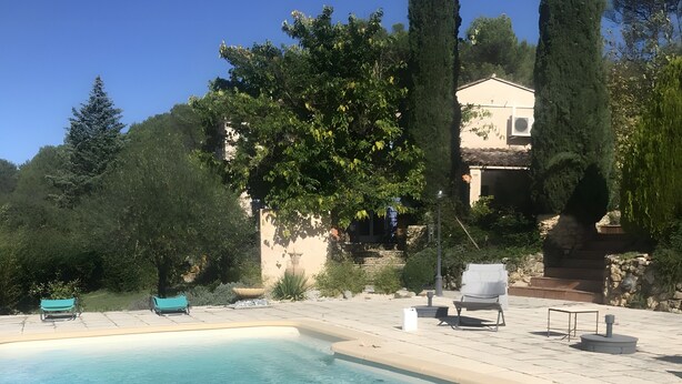 En swimmingpool med klart vand, omgivet af en patio med liggestole og en stenvæg.