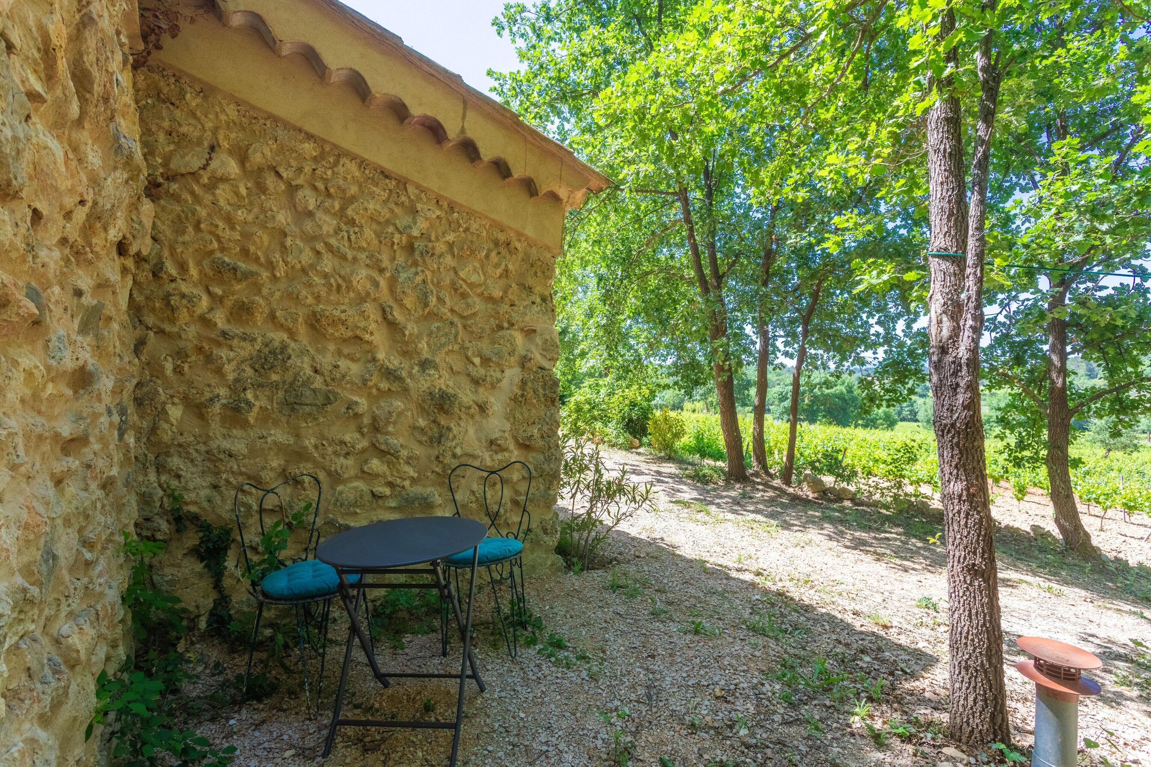 Un bâtiment en pierre avec une table et des chaises à l’extérieur, entouré d’arbres et de verdure.