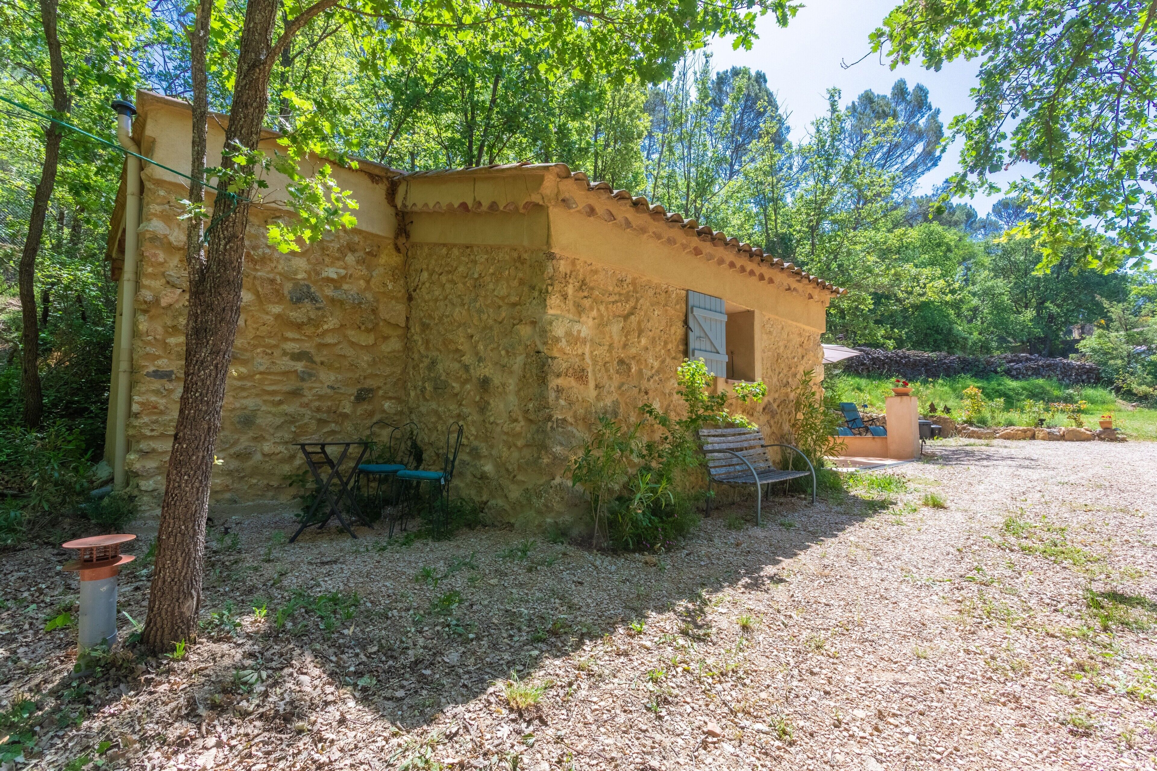 A rustic stone building with a tiled roof, surrounded by trees and a gravel path.