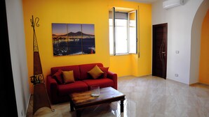 A living room with a red sofa, a coffee table, and a painting of a coastal cityscape. - Cozy apartment in the heart of the Spanish quarters (Napoli)