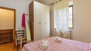 Een slaapkamer met een bed, een kledingkast, een stoel en een raam met gordijnen.
