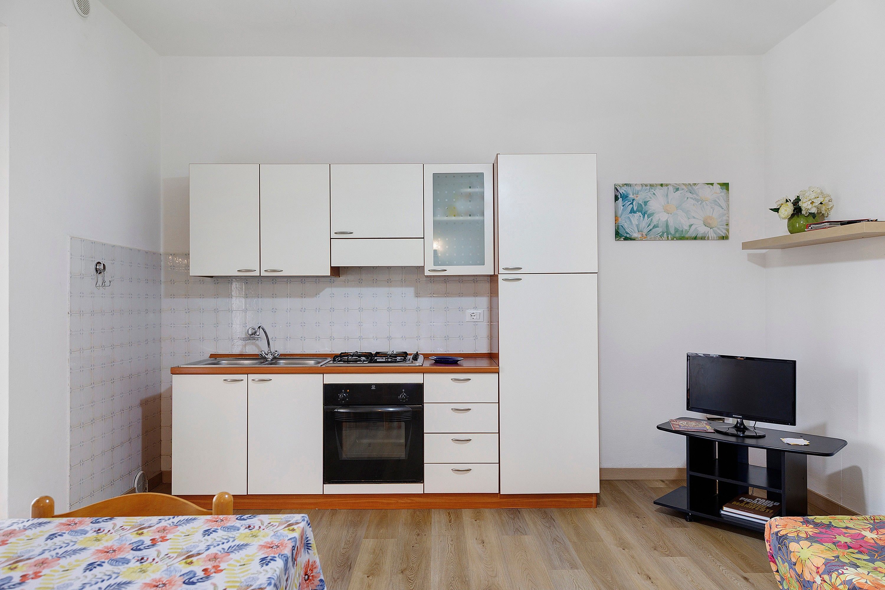 Cozinha compacta com armários brancos, fogão a gás e forno embutido.