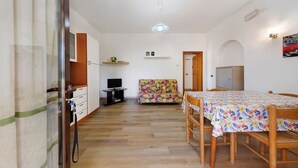 A dining area with a wooden table and chairs, a sofa, and a television. - Apartment 'Via Gorizia 8 - Verde' with Shared Garden, Wi-Fi and Air Conditioning (Cecina)