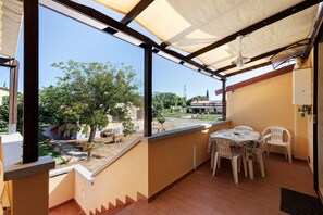 Un balcon avec une table et des chaises, une vue sur un jardin et un bâtiment en arrière-plan.