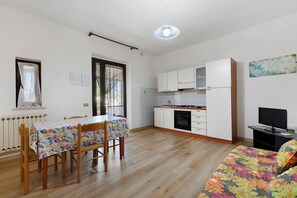 Une cuisine de taille réduite avec des meubles blancs, une table à manger avec des chaises, un canapé et un téléviseur.