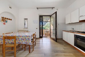 Une cuisine avec des meubles blancs, un plan de travail en bois et un coin repas agrémenté d’une nappe à motifs floraux.