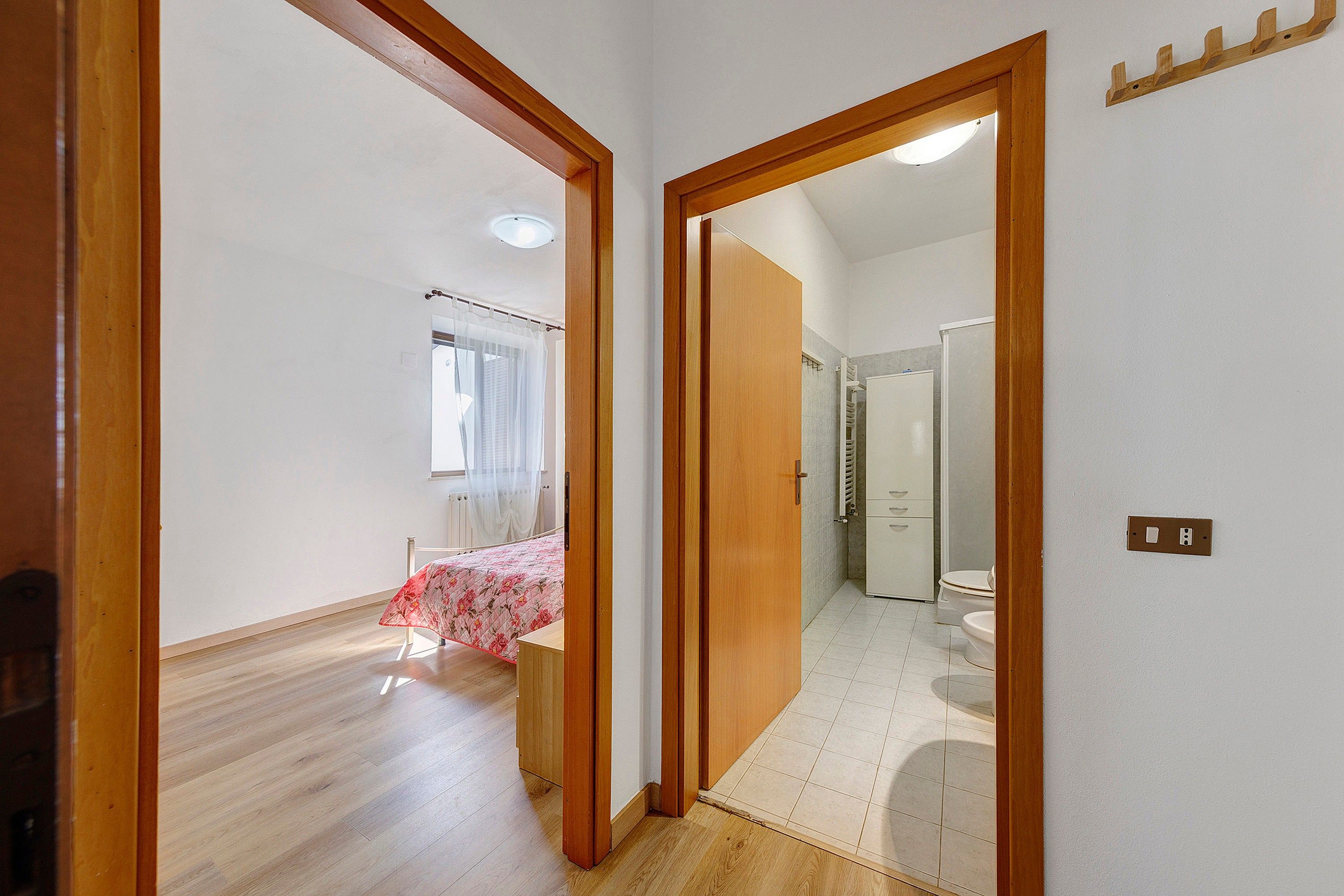 A hallway leading to a bedroom with a bed and a bathroom with a toilet and shower.